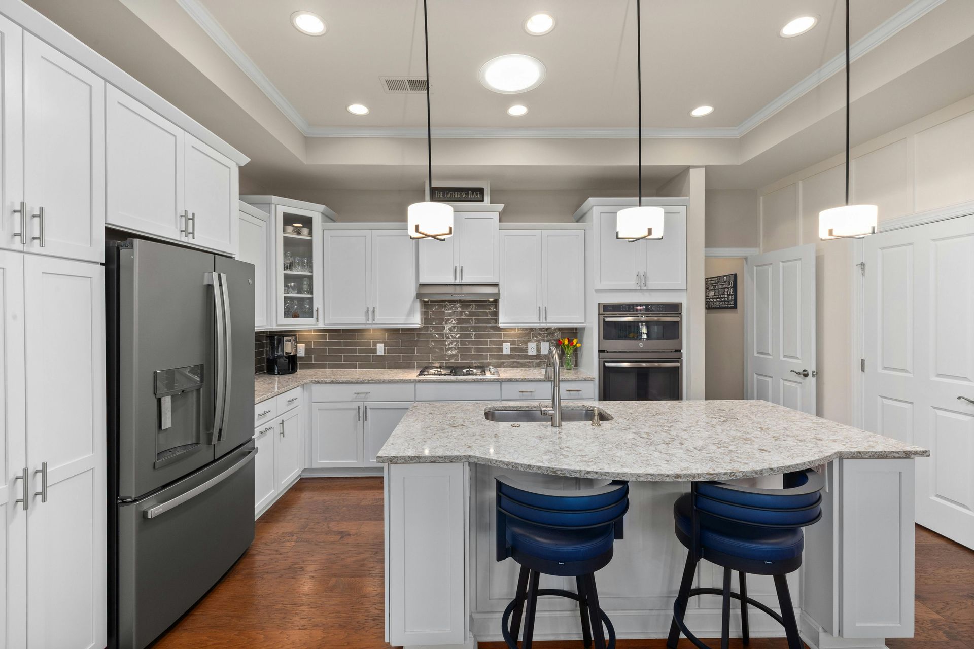 White shaker kitchen cabinets with a stone island, pendant lights and wall ovens